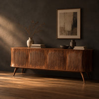 Long sideboard with vertical fluted doors on slim tapered legs, three-quarter view showing the grain