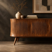 Corner detail of long sideboard with vertical fluted doors on slim tapered legs beside wood, brass and linen samples
