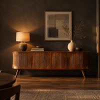 Long sideboard with vertical fluted doors on slim tapered legs in a dark dining room at golden hour