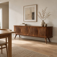 Long sideboard with vertical fluted doors on slim tapered legs in a Scandinavian dining room with white walls