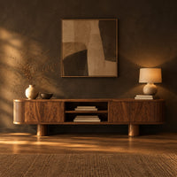 Low media stand with fluted ends, grain front panels and thick cylinder feet in a dark living room at golden hour