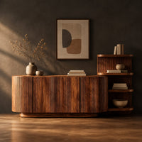Long fluted sideboard with curved ends and an open shelf tower at one end in a dark studio against a charcoal plaster wall