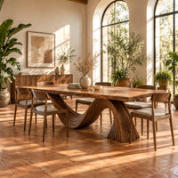 Dining table with a fluted wave shaped pedestal and rectangular top in a bright dining room with arched windows and plants