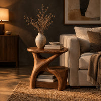 Forked branch side table with an oval top and open lower shelf in a dark living room at golden hour