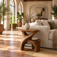 Forked branch side table with an oval top and open lower shelf in a bright living room with arched windows and plants