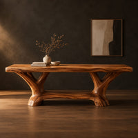 Rectangular dining table on two forked trunk legs joined by a low beam in a dark studio against a charcoal plaster wall