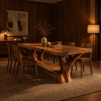 Rectangular dining table on two forked trunk legs joined by a low beam in an evening dining room with walnut wall paneling