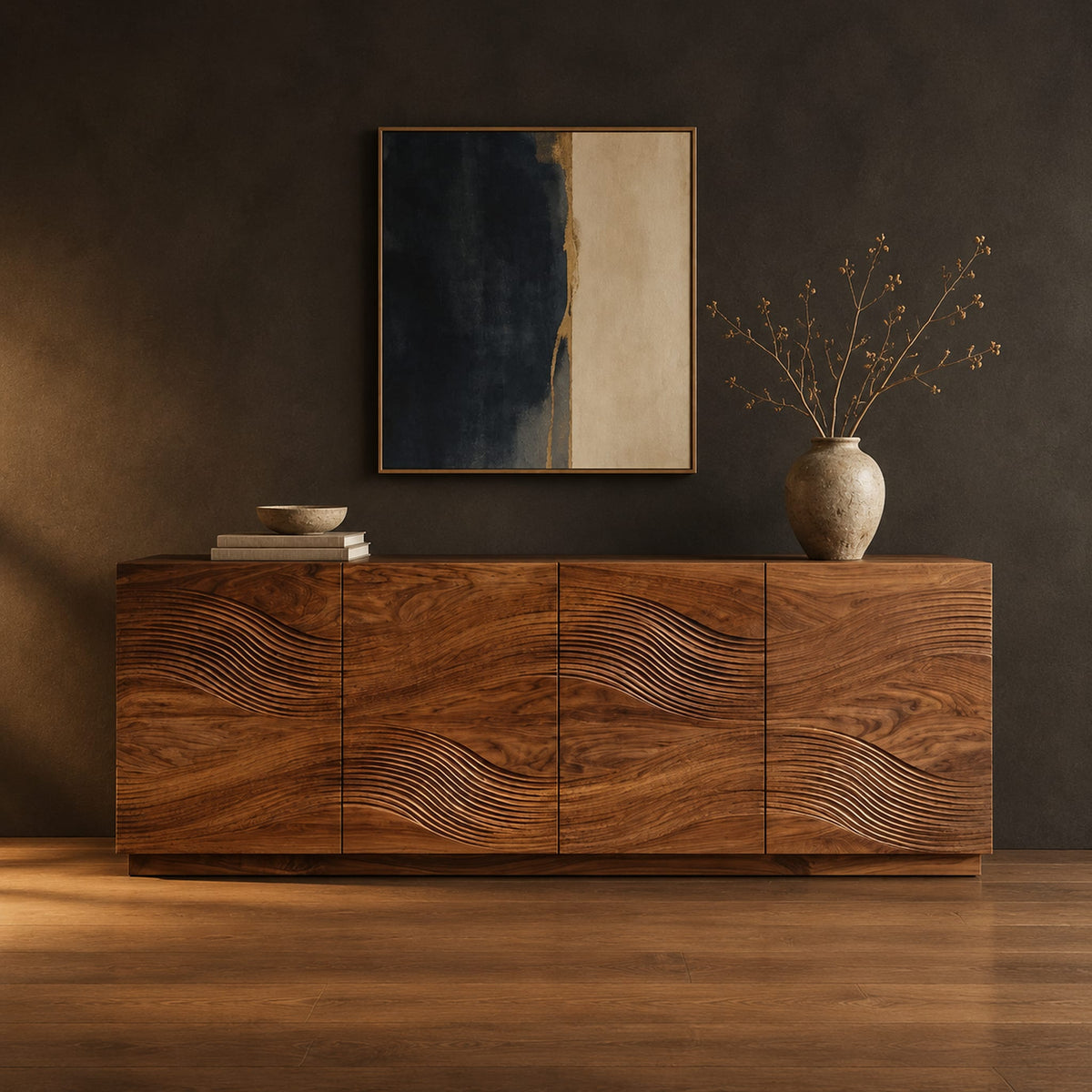 Four door sideboard with carved flowing wave lines on a plinth base in a dark studio against a charcoal plaster wall