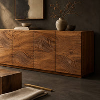 Corner detail of four door sideboard with carved flowing wave lines on a plinth base beside wood, brass and linen samples