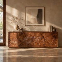Corner detail of tv stand with four doors carved with one ocean wave beside wood, brass and linen samples
