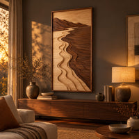 Framed wall art showing a carved river landscape in light and dark wood above a low console in an evening living room