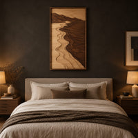 Framed wall art showing a carved river landscape in light and dark wood above a bed in a dusk lit bedroom