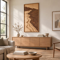 Framed wall art showing a carved river landscape in light and dark wood above a light oak sideboard in daylight