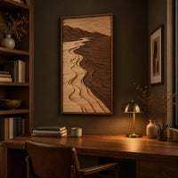 Framed wall art showing a carved river landscape in light and dark wood above a desk in a dark study corner