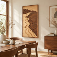 Framed wall art showing a carved river landscape in light and dark wood beside a dining table in natural light