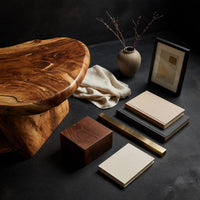 Corner detail of figured wood free form coffee table with a lower shelf beside wood, brass and linen samples