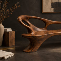 Corner detail of long freeform bench with oval cutouts along the back and flared legs beside wood, brass and linen samples