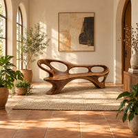 Long freeform bench with oval cutouts along the back and flared legs in a bright entryway with arched windows and plants