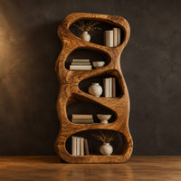 Freeform wooden bookshelf with five stacked pebble shaped open cells in a dark studio against a charcoal plaster wall