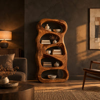 Freeform wooden bookshelf with five stacked pebble shaped open cells in a dark living room at golden hour