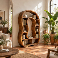 Freeform bookshelf with a keyhole shaped center opening and uneven shelves in a bright living room with arched windows and plants
