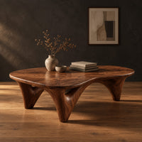 Freeform coffee table with a smooth organic top on sculpted arched legs in a dark studio against a charcoal plaster wall