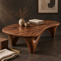 Corner detail of freeform coffee table with a smooth organic top on sculpted arched legs beside wood, brass and linen samples