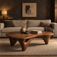 Freeform coffee table with a smooth organic top on sculpted arched legs in a dark living room at golden hour