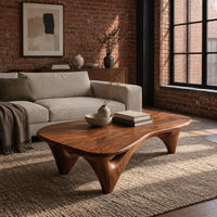 Freeform coffee table with a smooth organic top on sculpted arched legs in an industrial loft living room with exposed brick