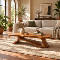 Freeform wooden coffee table with a sculpted branching base in a bright living room with arched windows and plants