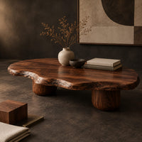 Corner detail of freeform coffee table with a wavy edged top and two thick cylinder legs beside wood, brass and linen samples