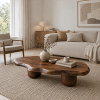 Freeform coffee table with a wavy edged top and two thick cylinder legs in a Scandinavian living room with white walls