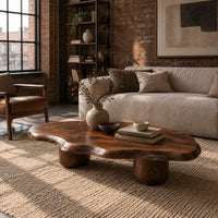 Freeform coffee table with a wavy edged top and two thick cylinder legs in an industrial loft living room with exposed brick