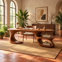 Oval wooden desk with a sweeping freeform base and two open shelf tiers in a bright home office with arched windows and plants