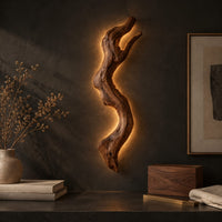 Corner detail of tall wall sconce shaped like a gnarled twisting branch with a glowing halo beside wood, brass and linen samples