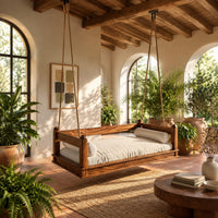 Hanging daybed swing with low wood rails and a thick seat pad in a bright porch with arched windows and plants