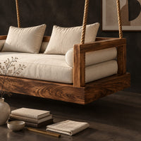 Corner detail of hanging daybed swing with a thick wood base and low frame sides beside wood, brass and linen samples