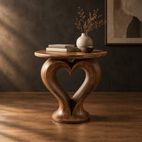 Round side table on a sculpted pedestal with a heart shaped opening in a dark studio against a charcoal plaster wall