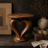 Corner detail of round side table on a sculpted pedestal with a heart shaped opening beside wood, brass and linen samples