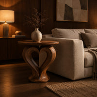 Round side table on a sculpted pedestal with a heart shaped opening in an evening living room with walnut wall paneling