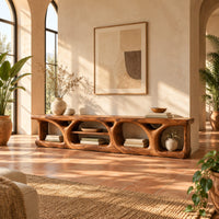 Long low media console with hollowed arch openings and open shelf bays in a bright living room with arched windows and plants