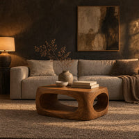 Chunky block coffee table with large oval tunnel openings through its sides in a dark living room at golden hour