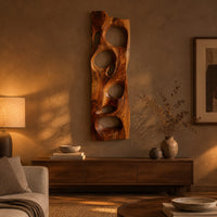 Wooden wall art panel with irregular oval cutouts above a low console in an evening living room