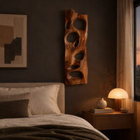 Wooden wall art panel with irregular oval cutouts above a bed in a dusk lit bedroom