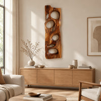 Wooden wall art panel with irregular oval cutouts above a light oak sideboard in daylight
