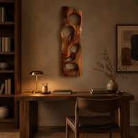 Wooden wall art panel with irregular oval cutouts above a desk in a dark study corner