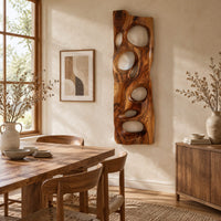 Wooden wall art panel with irregular oval cutouts beside a dining table in natural light
