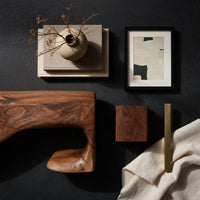 Corner detail of dark coffee table with a scooped hollow and hooked end beside wood, brass and linen samples
