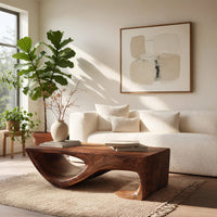 Dark coffee table with a scooped hollow and hooked end in a sunlit room with large windows and plants