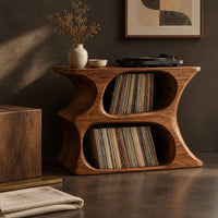 Corner detail of hourglass record player stand with two stacked oval openings and a flat top beside wood, brass and linen samples